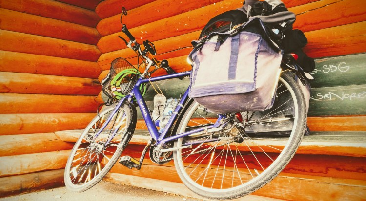 A bicycle hanging by it's right pedal on a wooden bench in a bus stop