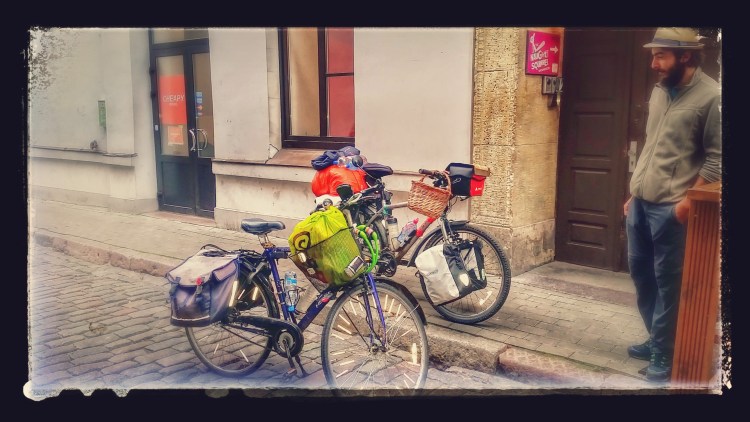Two bicycles parked in a small street with a men looking at it